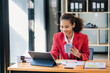 © Nuttapong punna - Confident beautiful Asian businesswoman typing laptop computer and digital tablet while holding coffee at office..