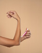 © vladimirfloyd - A woman shaves her arms with a disposable pink razor on a beige background