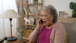 korean grey haired grandma answering scam call from a stranger is feeling shocked at the bad news over the mobile phone in the living room at home