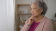 closeup shot of a worried asian senior female keeping hand on the chin and shaking head with a sigh while considering a decision in the living room at home