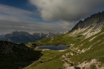 Sticker - Green valley and Lake Olbe in mountainous environment under dense clouds reflected in water, Italy