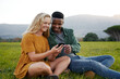 © StratfordProductions - Happy multiracial young couple sitting and using mobile phone in field