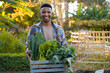 © StratfordProductions - Happy young black man smiling while looking at camera with vegetable harvest in plant nursery