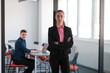 © .shock - Portrait of young smiling business woman in creative open space coworking startup office. Successful businesswoman standing in office with copyspace. Coworkers working in background.