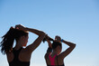 Fitness women, silhouette and blue sky background of runner tying hair together after outdoor run, cardio exercise and wellness health. Healthy running girls, sports athlete and friends morning run