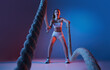 © master1305 - Young sportive girl training with sports equipment, ropes isolated over gradient blue purple studio background in neon light. Power