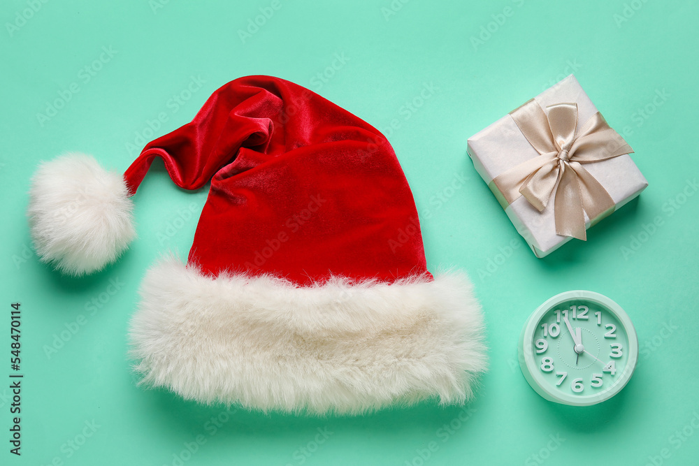 Santa hat, Christmas gift and alarm clock on color background