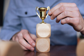 Wall Mural - Business person arranging large wooden blocks with a winning trophy. Business success