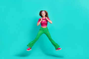 Poster - Full length photo of dreamy cheerful schoolgirl wear pink crop top flare trousers listening songs jumping high isolated turquoise color background