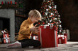 © somemeans - Happy child opens big Christmas gift on Christmas tree background. Joyful boy with Xmas present. New Year time.