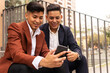 © ADDICTIVE STOCK - Cheerful Hispanic men using smartphone outside
