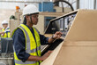 © Supachai - Young African American male engineer in vest and helmet safety checking and repairing old CNC machinery at factory Industrial.