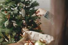 Hands Decorating Christmas Tree With Stylish Bauble In Atmospheric Festive Room. Merry Christmas! Winter Holidays Preparation. Woman In Cozy Sweater Putting Vintage Star On Tree