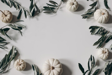 Wall Mural - Autumn floral decorative frame, border. White little pumpkins and olive tree leaves and branches isolated on table background. Seasonal banner for Thanksgiving, Halloween. Winter holiday flat lay, top