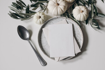 Wall Mural - Autumn stationery still life. White little pumpkins, olive tree leaves, branches isolated on table background. Greeting card, invitation mockup. Ceramic plate, vintage spoon. Thanksgiving, Halloween