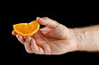 Piece of orange in hand isolated on black