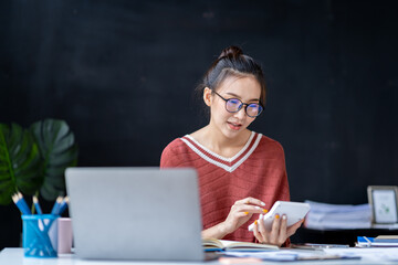 Portrait of an Asian businesswoman pressing a calculator, looking at a notebook, analyzing data, and reports, preparing presentations, marketing, and finance for sales in online shopping systems.