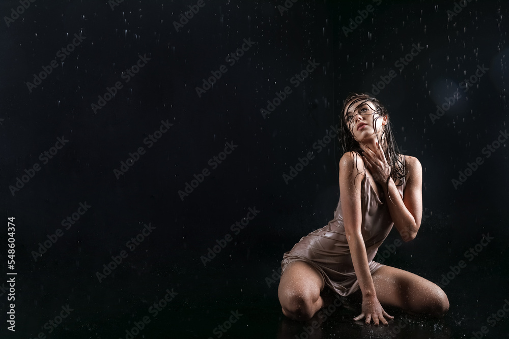 Attractive young woman with dripping water sitting on black background
