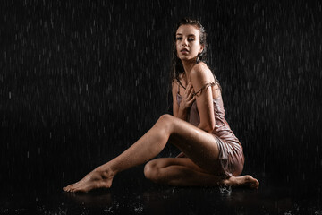 Wall Mural - Attractive young woman with dripping water sitting on black background