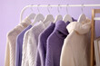 © Pixel-Shot - Rack with knitted sweaters near lilac wall, closeup