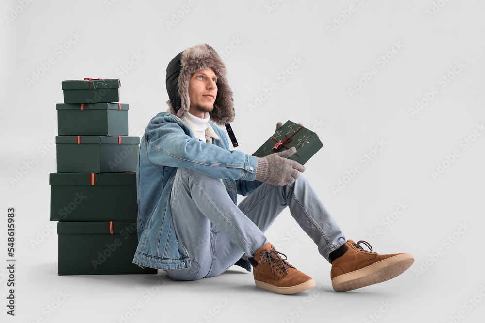 Handsome man with Christmas presents sitting on light background