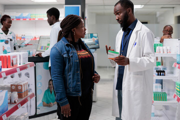 African american man pharmacist recommending woman food supplements in drugstore. Medicaments retail, client and pharmacy store consultant talking, buyer choosing vitamin c, all black team