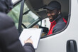 © PoppyPix - Happy positive Black courier joking around with unrecognizable person taking a delivery. Unrecognizable person signing delivery documents standing next to white delivery truck. High quality photo