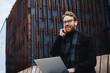 © YURII MASLAK - Successful businessman background of the business center. A red-haired young guy, in a stylish coat, wireless headphones with a laptop, holds an online call, consultation, interview. Remote control.