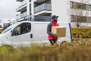 Wall Mural - The use of vehicles in package delivery. Outdoor shot of handsome Black deliveryman in front of his white truck walking towards client's house. Blurred foreground. High quality photo