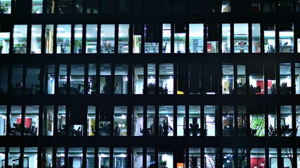 Wall Mural - Modern office building in city at the night. View on illuminated offices of a corporate building. Blinking light in window of the multi-storey building of glass and steel. Long exposure at night