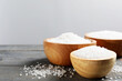 Bowls of natural sea salt on grey wooden table, space for text