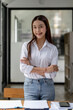 © NAMPIX - Portrait of young smiling woman looking at camera with crossed arms. Happy girl standing in creative office.