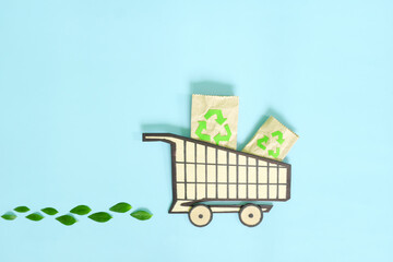 Environment friendly, sustainable, ecological shopping or consumerism and carbon footprint reduction concept. Shopping cart icon with fresh green leaves creative flat lay.