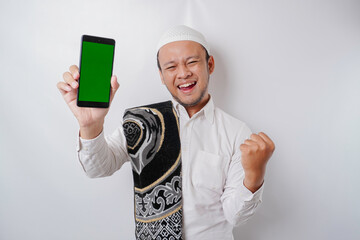 A happy young Asian Muslim man with a successful expression showing copy space on his phone isolated by white background