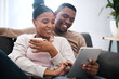 © T Hover/peopleimages.com - Digital tablet, relax and black couple on a sofa scrolling on social media, mobile app or the internet. Happy, smile and African man and woman reading messages together on a device in the living room
