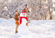 © JenkoAtaman - Happy children brother and sister making snowman together while playing with snow in winter park
