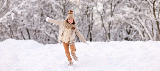 Wall Mural - Happy excited little girl playing in winter park, kid running through snow with arms outstretched