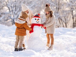 Sticker - Happy family mother and two little kids making snowman together in winter park outdoors