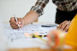 © bongkarn - Asian male engineer holding pen, working on a blueprint, checking scale, planning building process.
