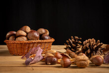 Close-up Of Basket With Chestnuts And Nuts With Autumn Leaves On Wooden Table, Black Background, Horizontal, With Copy Space