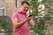 © sommersby - Millennial man using smartphone shocked by reading online news, frowning guy holding cell phone see warning notification. Confused guy looks at phone screen in surprise and stands outside at summer.