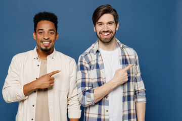 Wall Mural - Young two friends men wear white casual shirts together point index finger aside indicate on workspace area copy space mock up isolated plain dark royal navy blue background. People lifestyle concept.
