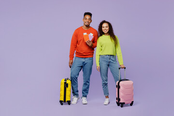 Full body fun young couple friends man woman in casual clothes together hold passport ticket bag isolated on plain purple background. Tourist travel abroad in free time rest. Air flight trip concept.