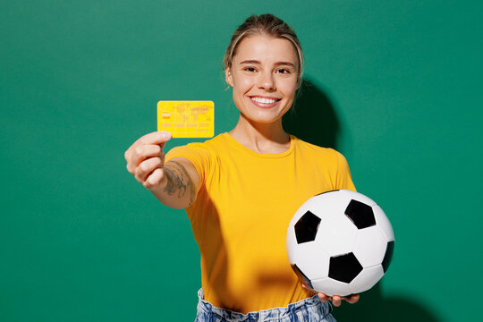 Young fun woman fan wear basic yellow t-shirt cheer up support football sport team hold soccer ball yellow card propose player retire from field watch tv live stream isolated on dark green background.
