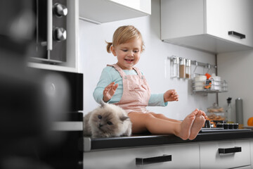cute little child sitting with adorable pet on countertop in kitchen