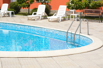 Wall Mural - Outdoor swimming pool with handrails and empty sunbeds at resort on sunny day