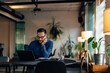 © bnenin - Businessman sitting alone at the office, holding hand on his cheek, using a laptop.