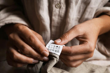 woman holding clothing label on beige garment, closeup