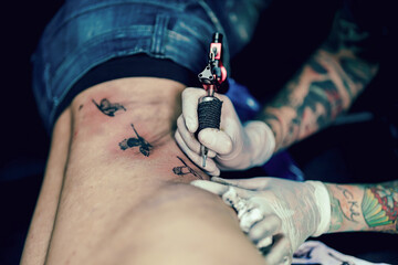 Professional tattooist makes the tattoo on a men waist, in a modern studio lowlight.