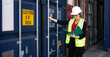 Female foreman supervisor wears safety hardhat inspecting container cargo at warehouse storage terminal. Industrial engineer woman works outdoors at international import export distribution facility.